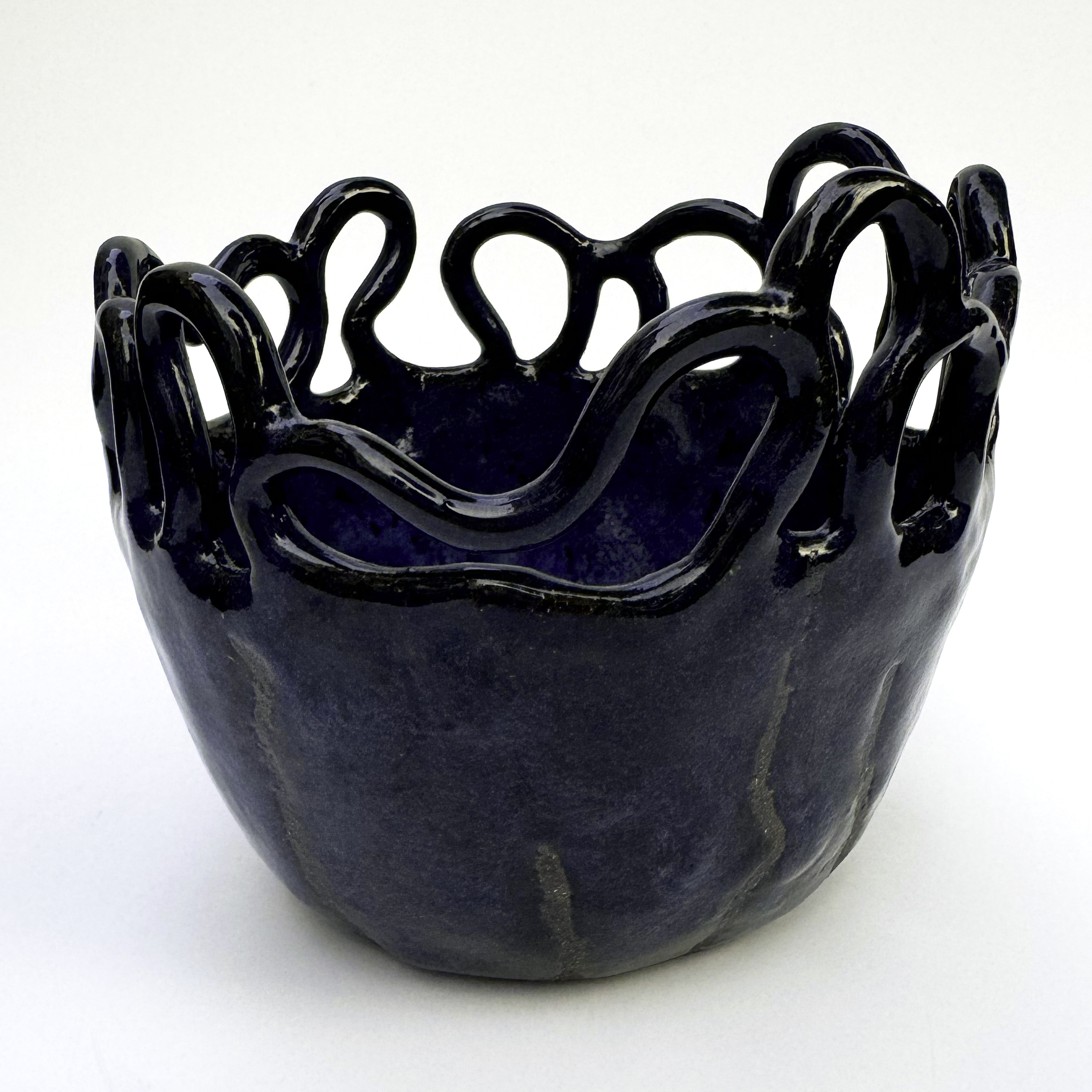 Thin, hand drawn lines from the coiled structure at the rim to the base of the bowl remain unglazed, revealing a matte black stoneware body.