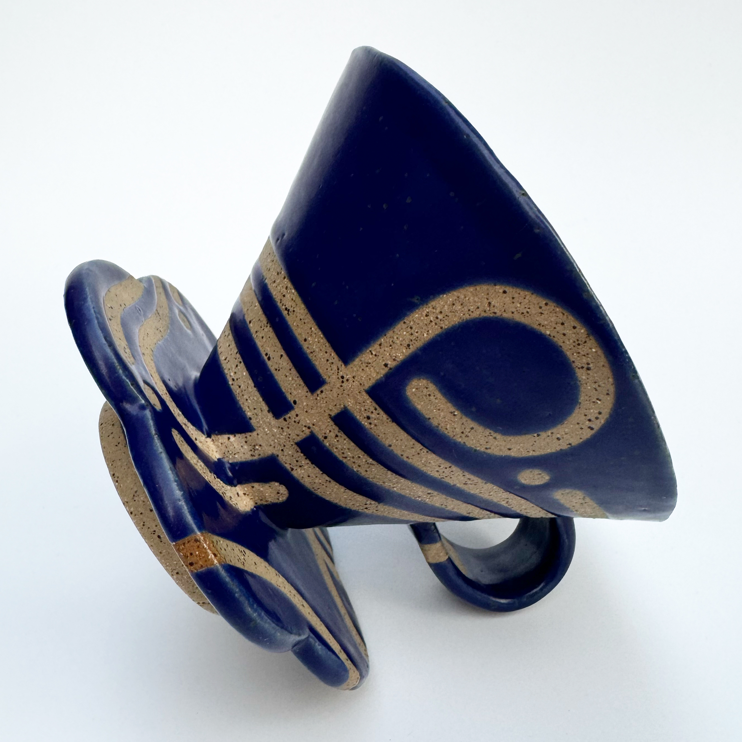 A handled V60-style coffee cone is covered in satin bright blue glaze except for various swirling lines that spread across the outside to reveal the black speckled tan clay.