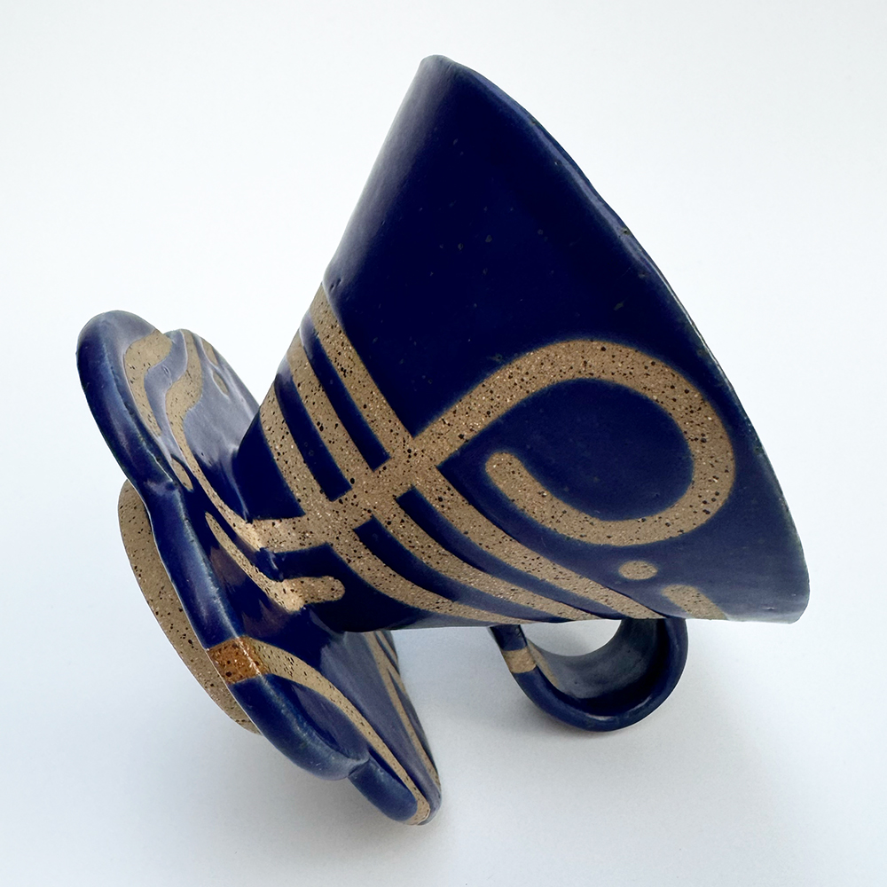 A handled light tan V60-style coffee cone with speckles is glazed in bright blue with swirls and spirals left bare.