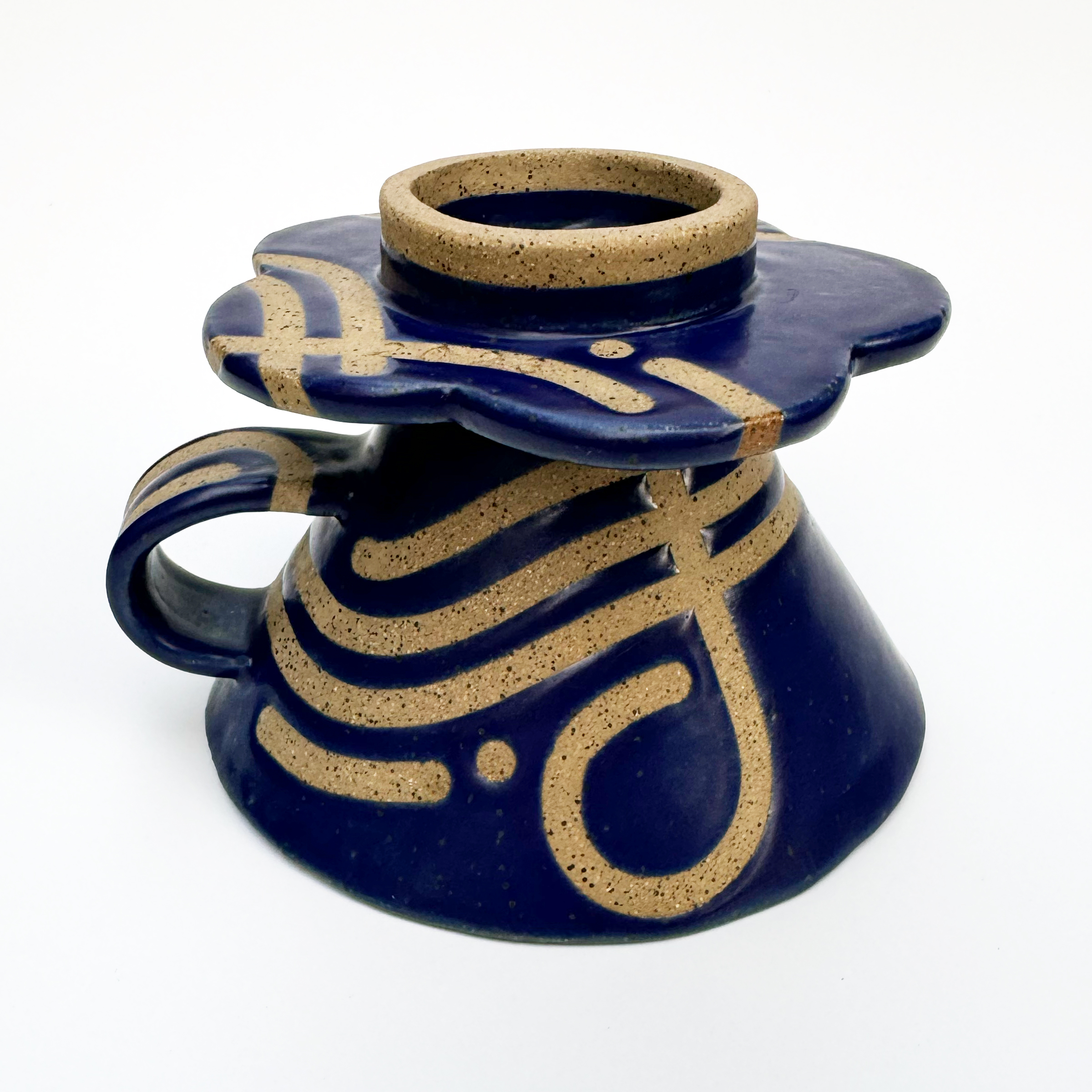 The base that rests atop a coffee cup or pitcher has a 5-petaled daisy shape, and the tape-resist blue glaze design continues along the bottom.