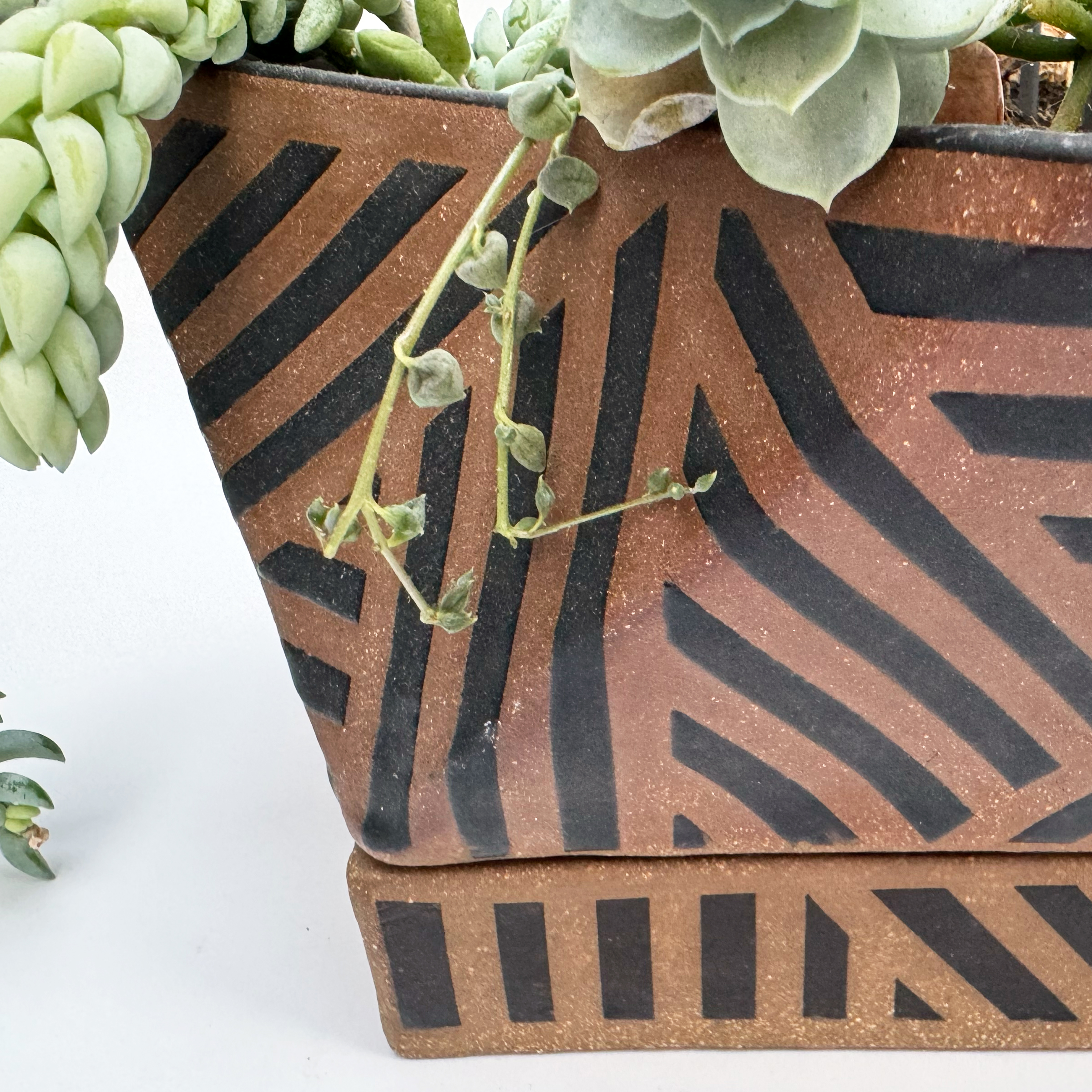 Matte black glaze is applied in many sets of straight lines that go in many directions following the planter's geometric form.