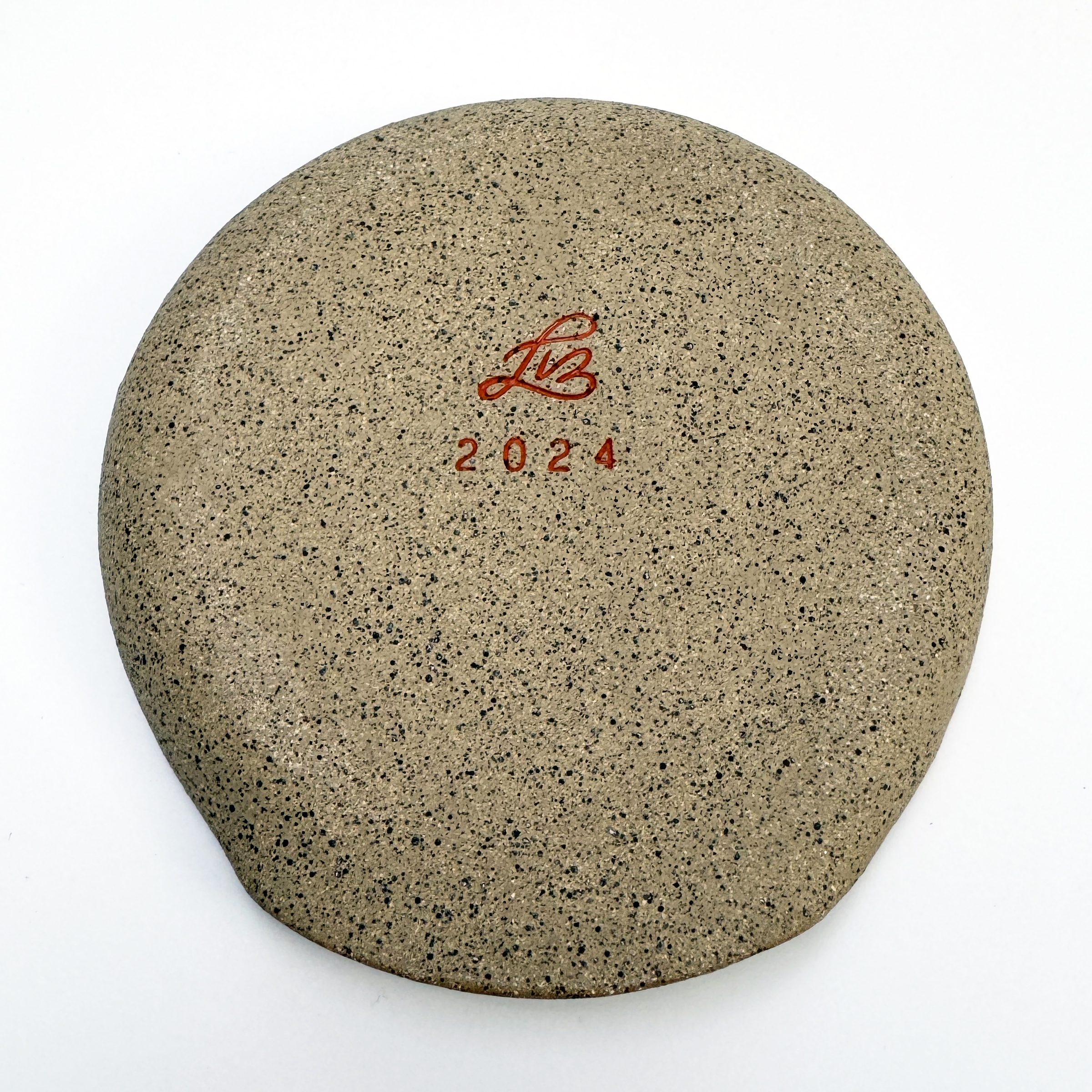 The edges and the bottom are unglazed to show off the raw tan stoneware clay and its speckles. The bottom is completely smooth and has no foot. Translucent orange gloss glaze is in the signature.