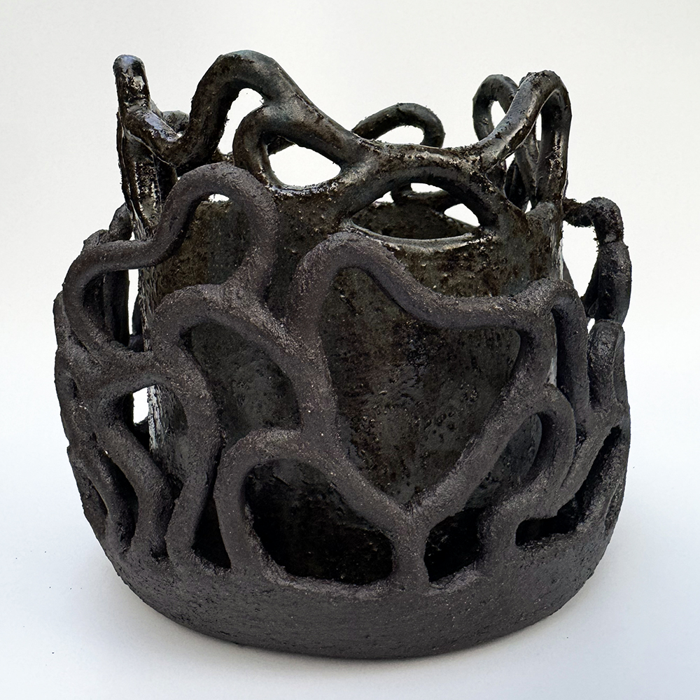 A rough textured black planter with a coral coil structure attached to the rim of the planter and its attached drip tray. The coils attached to the drip tray create an irregular mesh around the body of the planter.