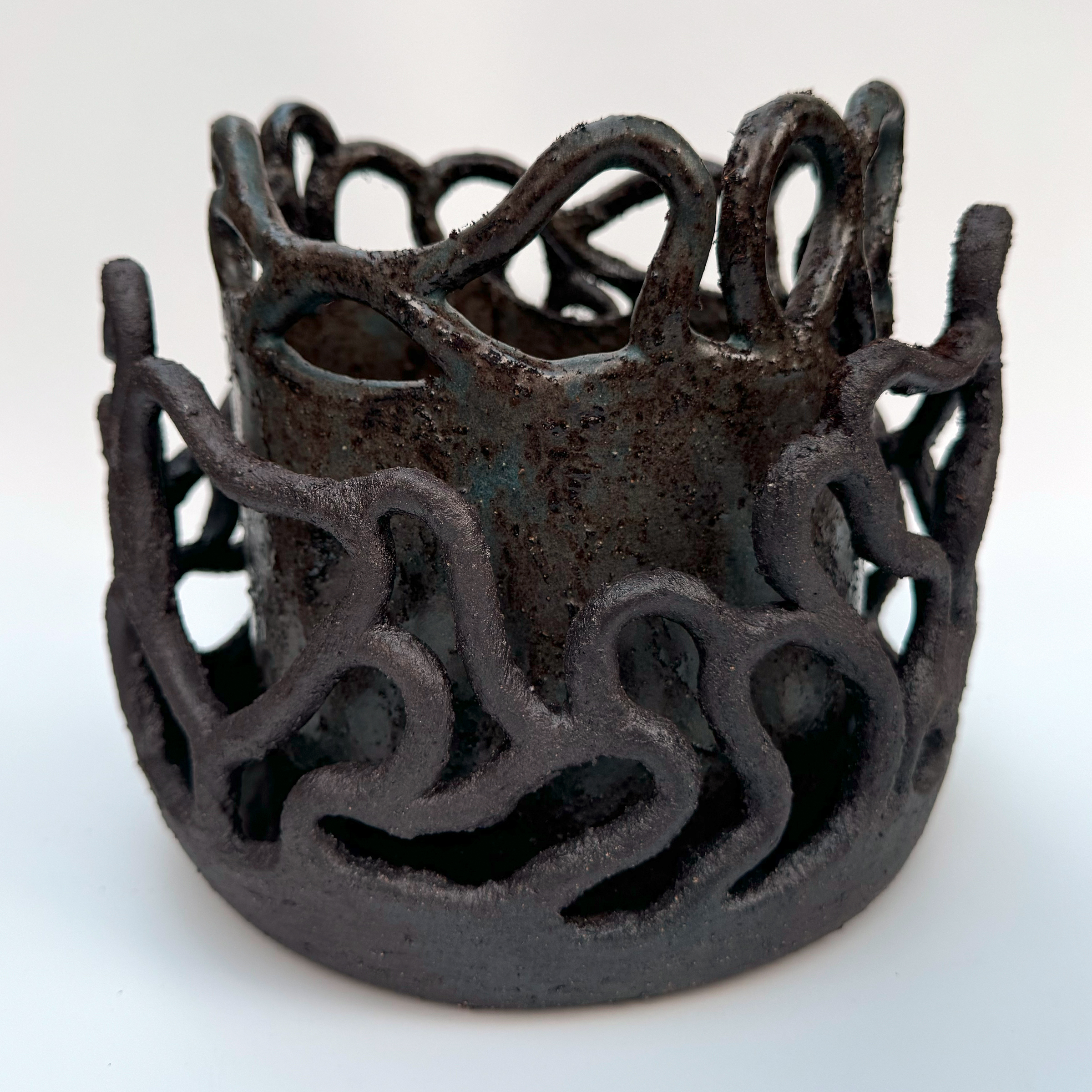 A wall of unglazed coils connected to the rim of the drip tray make a coral-like sculpture that surrounds the body of the planter.