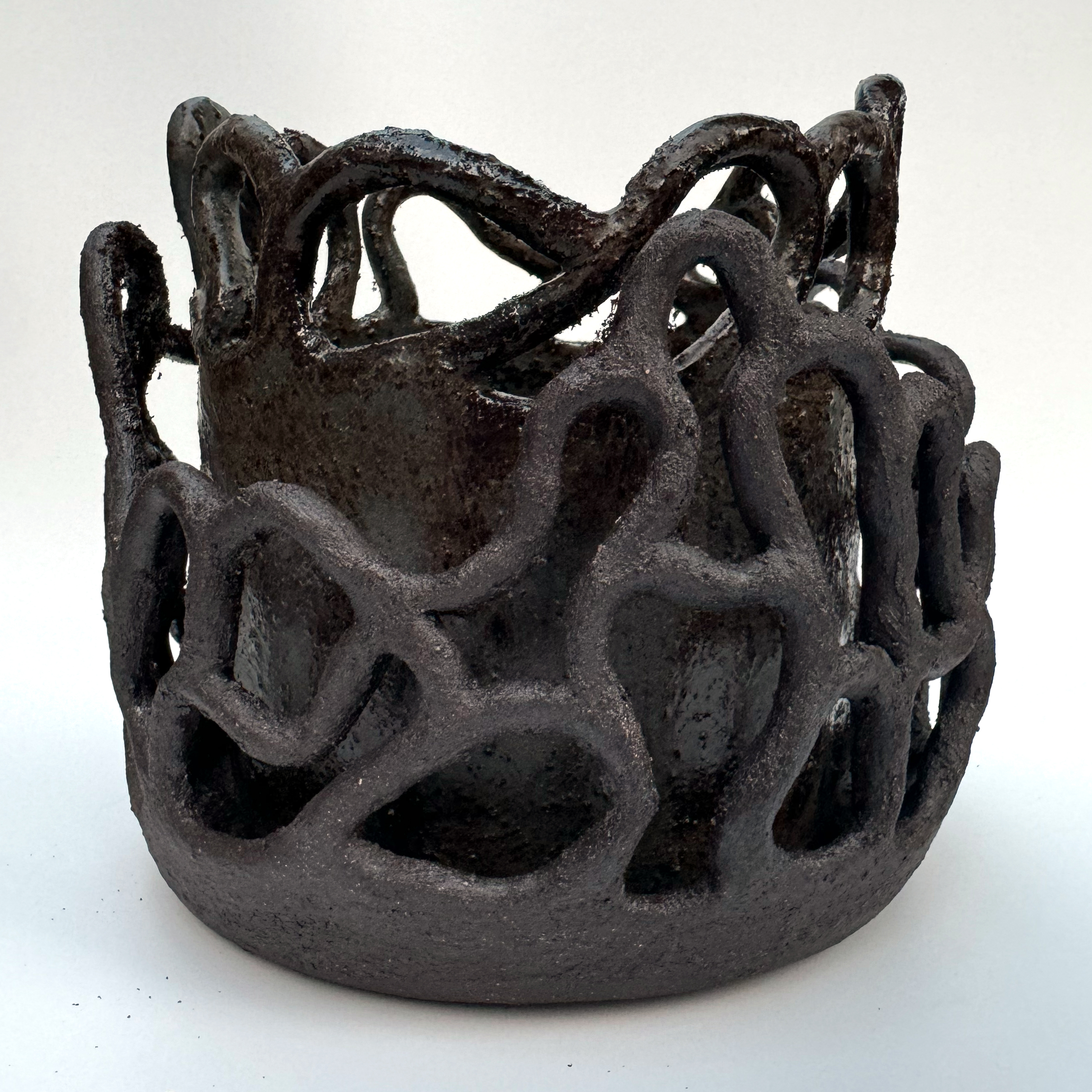 The raw, unglazed black stoneware coils surrounding the planter are arranged in a random pattern. They are more matte than the body of the planter.