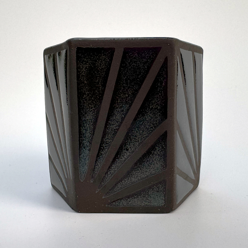 Hexagonal teacups in a black stoneware have a starburst-like pattern made of denim glaze on their sides.