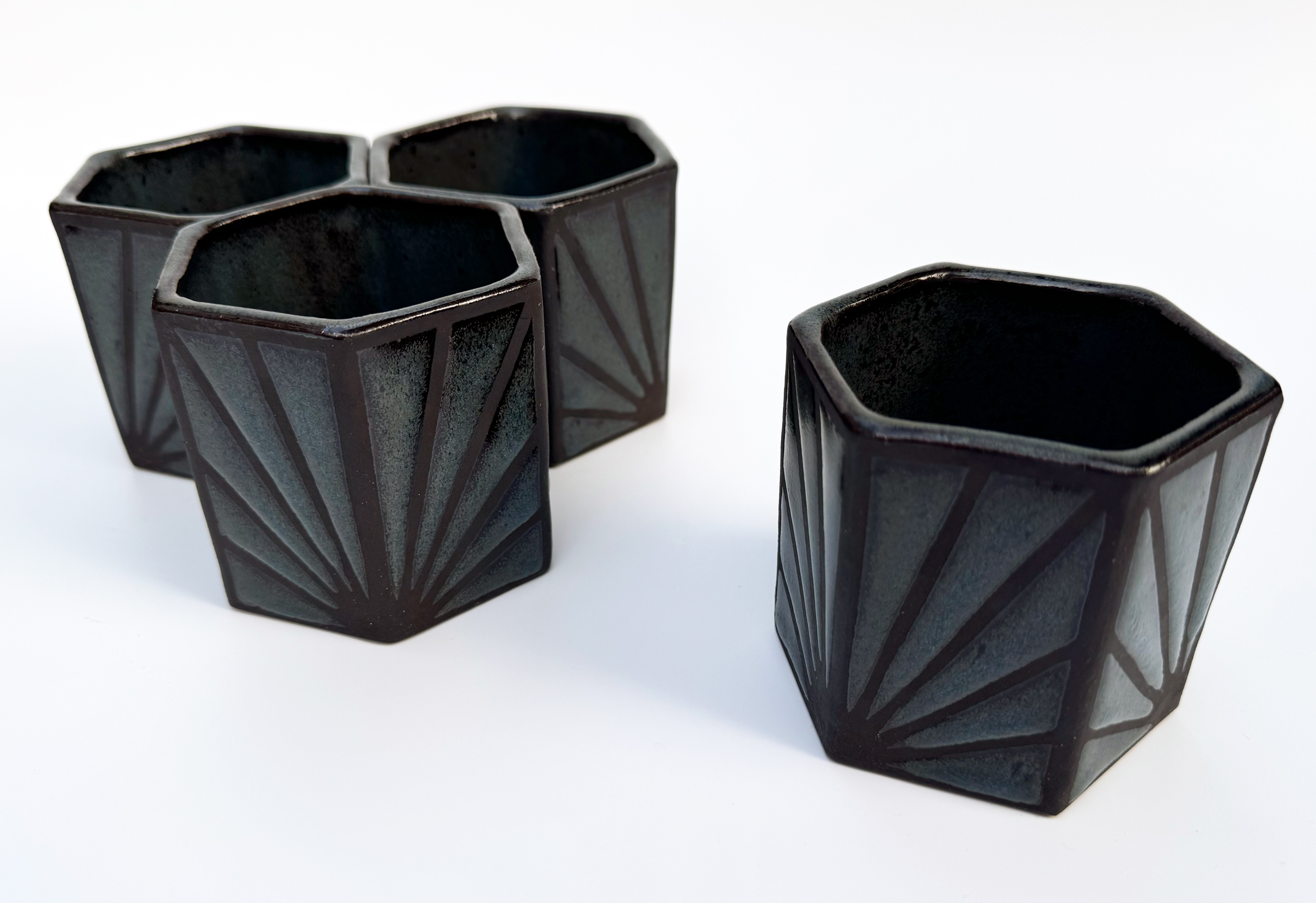 These black stoneware teacups have hexagonal bottoms and openings and six straight sides.