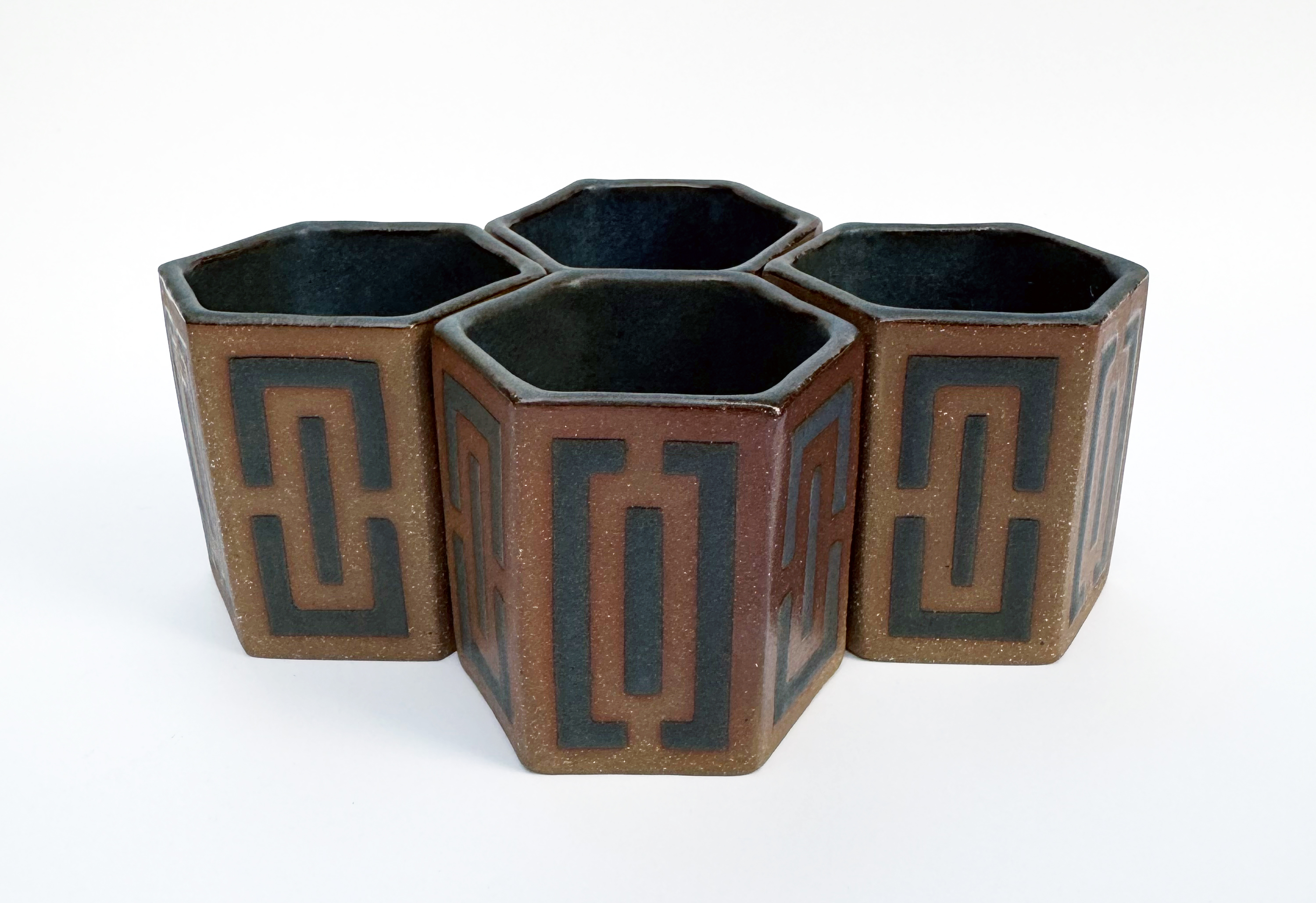 These medium brown stoneware teacups have hexagonal bottoms and openings and six straight sides.