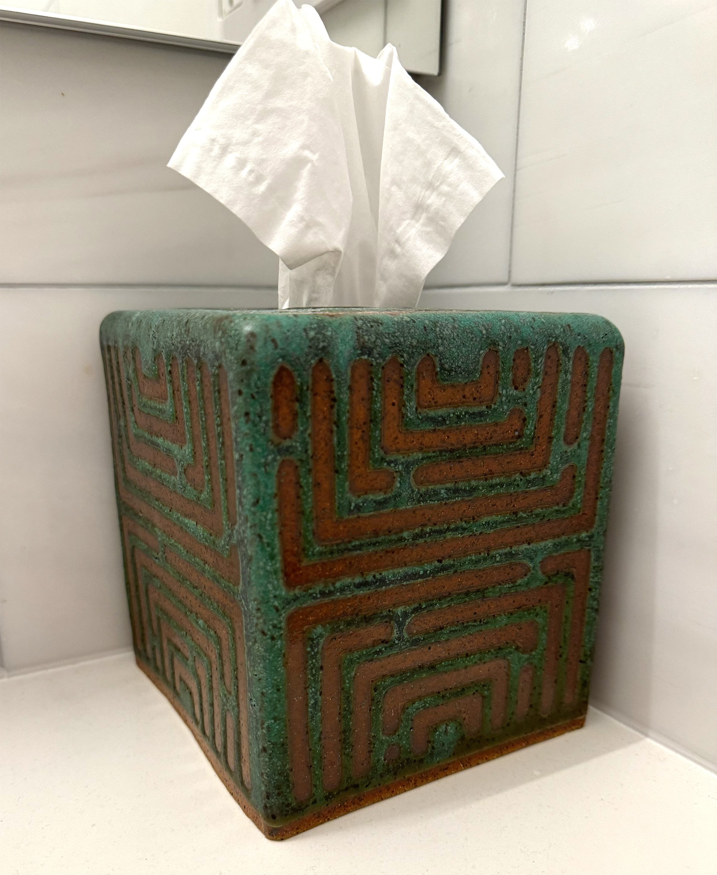 A tissue box has a maze-like pattern in black speckled matte green glaze reminiscent of tarnished copper.