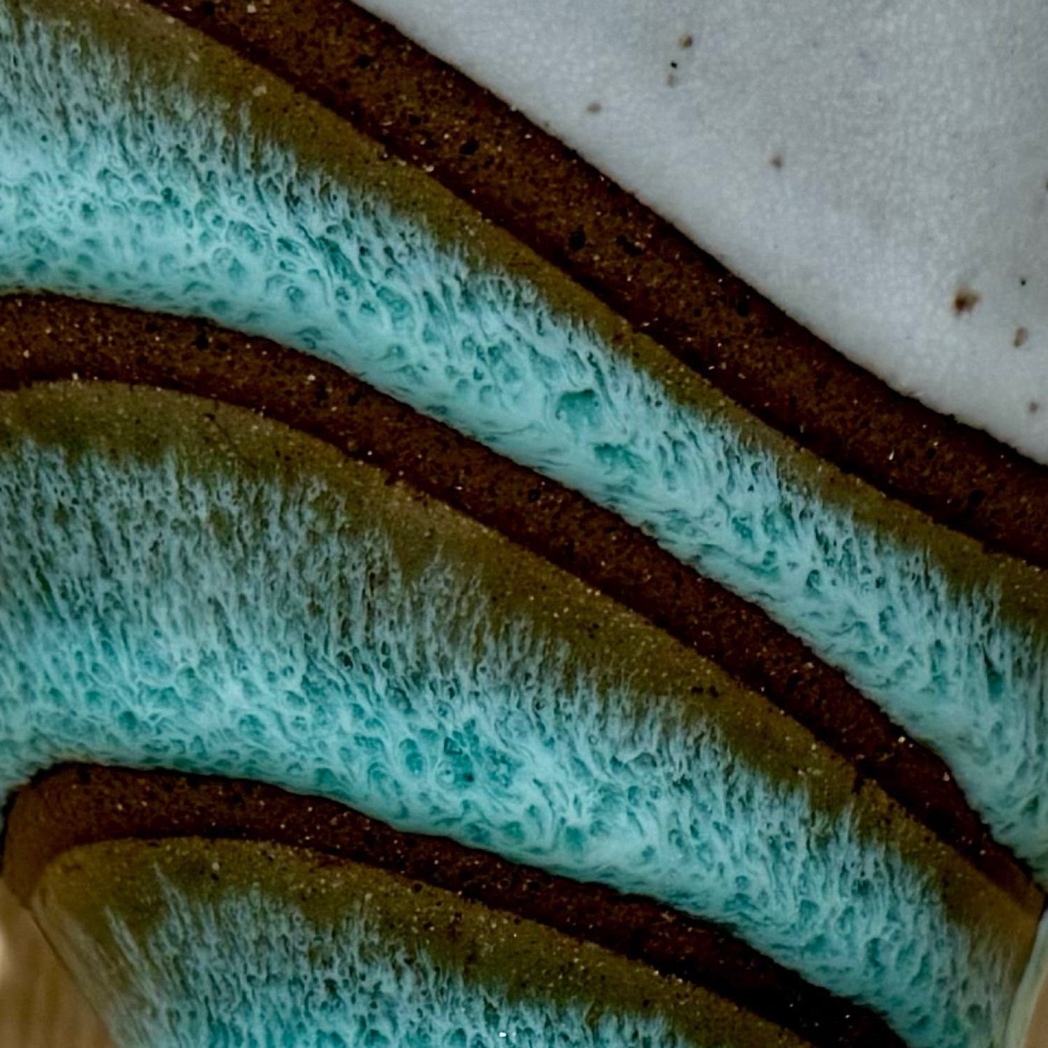 Drippy layers of glaze on a pot evoke sea foam hitting the beach - layers of sea foam aquas with white streaks breaking over them against dark tan speckled clay.