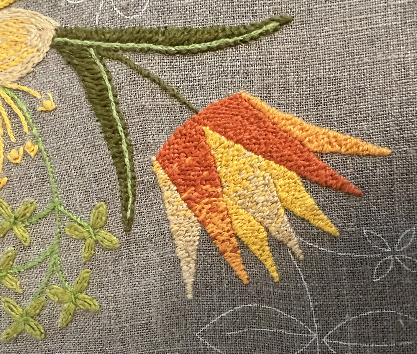 A flower shaped like the side view of a pointed crown is done in a small backstitches with red, orange, yellow, and light peach threads so that it looks almost like it's pixellated. Most petals are a pixelated gradient from one color to another, but some are just small backstitches in a single color. Two thin leaves are done in otomi stitch in olive green with a lime green stem stitched line down their spine.