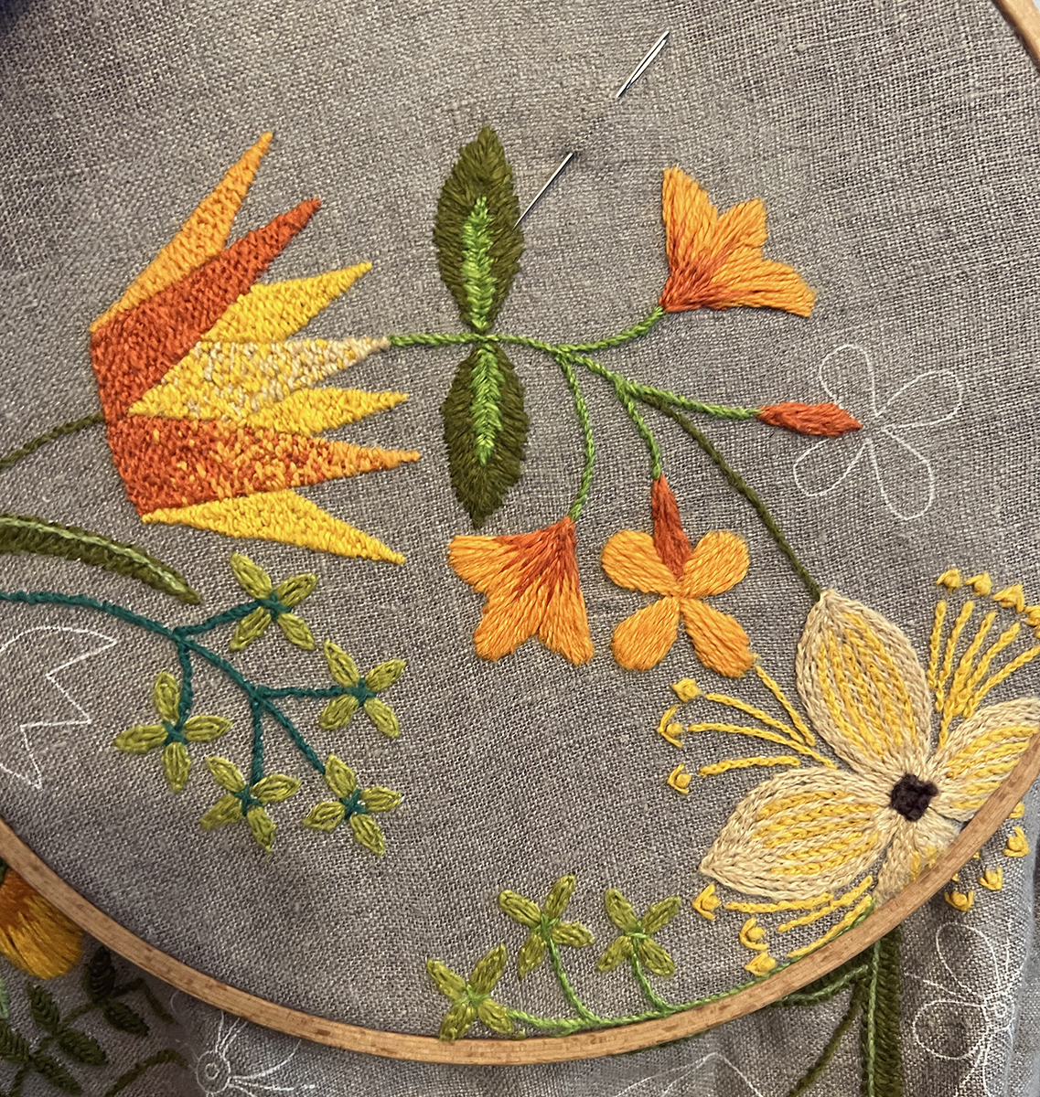 A flower shaped like the side view of a pointed crown is done in a small backstitches with red, orange, yellow, and light peach threads so that it looks almost like it's pixellated. Small orange flowers in satin stitch blend to bright red orange near their stems. Small entire leaves are stitched in two tones of green satin stitch. Small light lime green four-petaled flowers are done in two layers of lazy daisy stitch. A four-petaled light peach flower is done in split stitch with yellow chain stitch lines through the middle, and yellow chain stitch filaments and stamens emerge from the center, too.