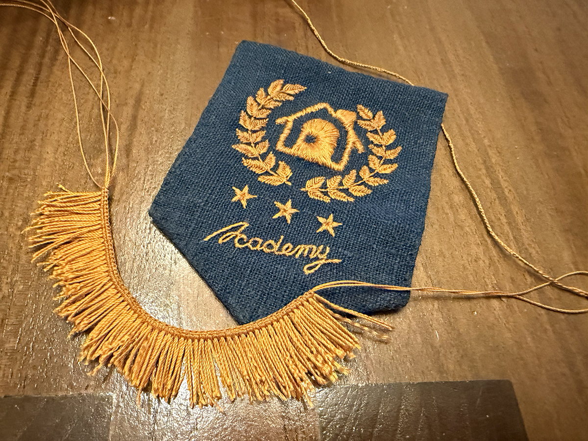 A long cord of macrame square knots with lark's heads attached to the bottom side next to the in-progress pennant. The lark's head dangles are uneven lengths at this phase because I didn't cut them until I was otherwise fully done with the project, and the base underneath the square knots hasn't been cut short so that I could hide them in edge wrapping. 