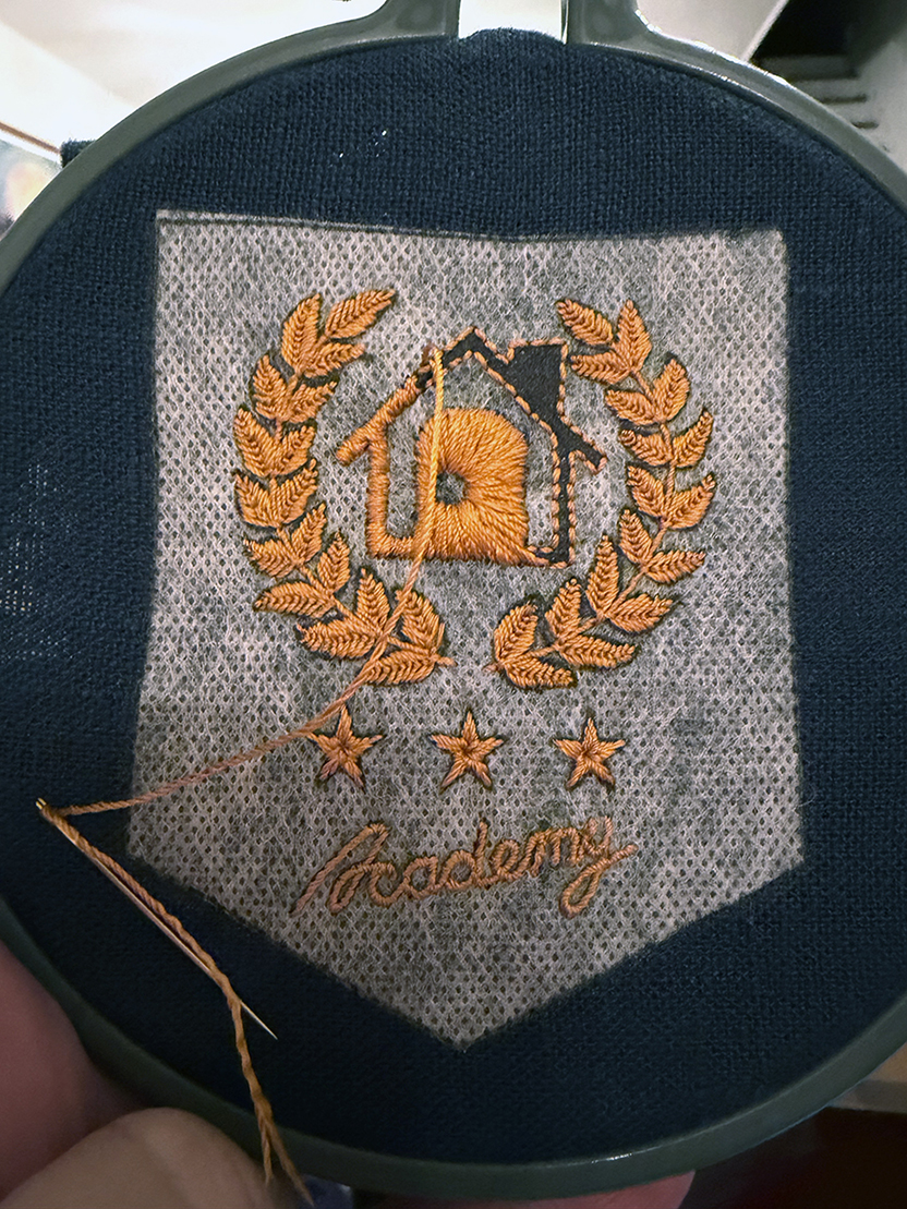 The house outline and filled in door are stitched in a satin stitch that is oriented towards the empty hole that serves as the door's handle.