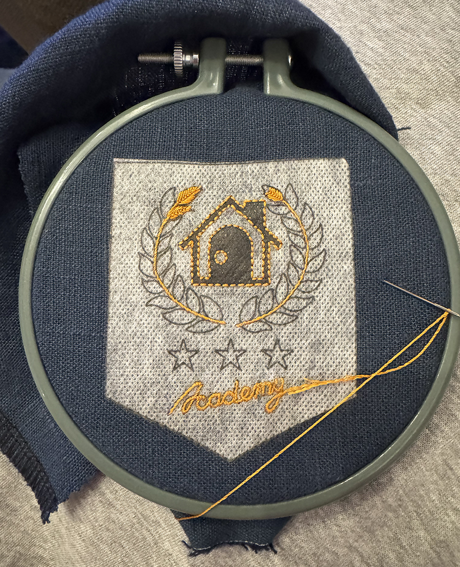 Stem stitches make up the branches for the laurel wreaths and word 'Academy' on top of my Sulky Fabri-Solvy template that's affixed to the the inky blue linen which is inside a small plastic hoop.