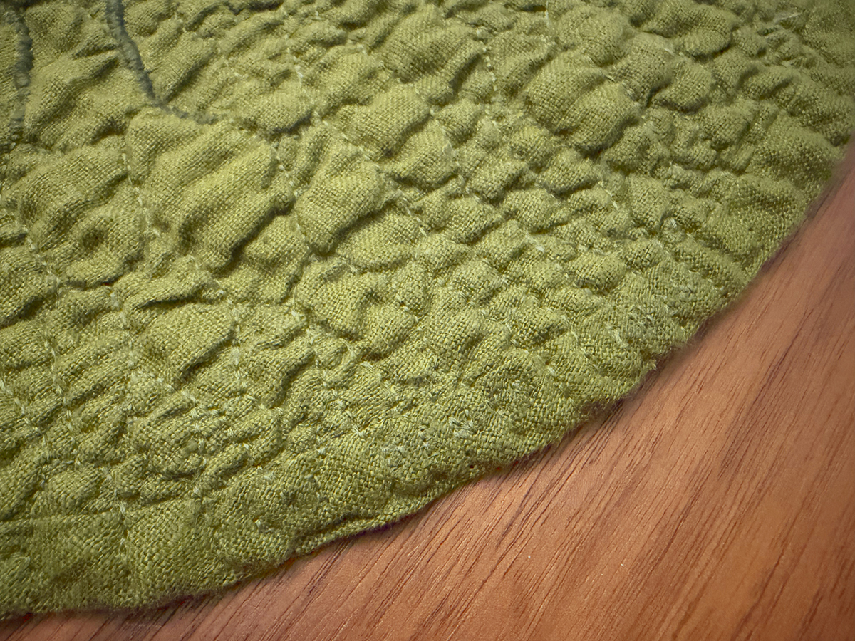 The edges are finished in bias tape, but instead of having a very defined edge without quilting, I continued the quilting vein pattern over the bias tape as well. I also stitched in my name and the year 2026 along the bias tape edge in this section.