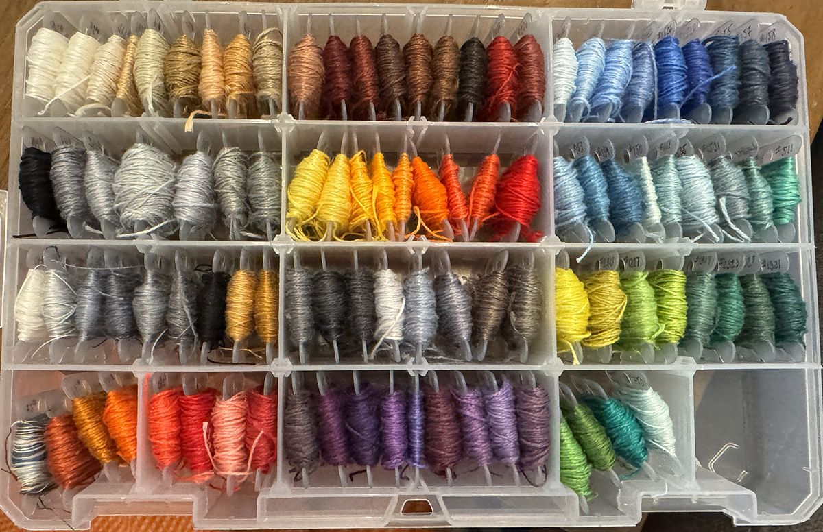97 colors of linen thread on bobbins are in a bin - every color of the rainbow is represented in multiple shades alongside a lot of blacks, greys, whites, beiges, and browns. 96 of the threads are a single color, though there are slight variations in the dye in some of them, and the last of the threads is a fine thickness space-dyed thread that includes orange, copper, grey, white, teal, and navy tones.