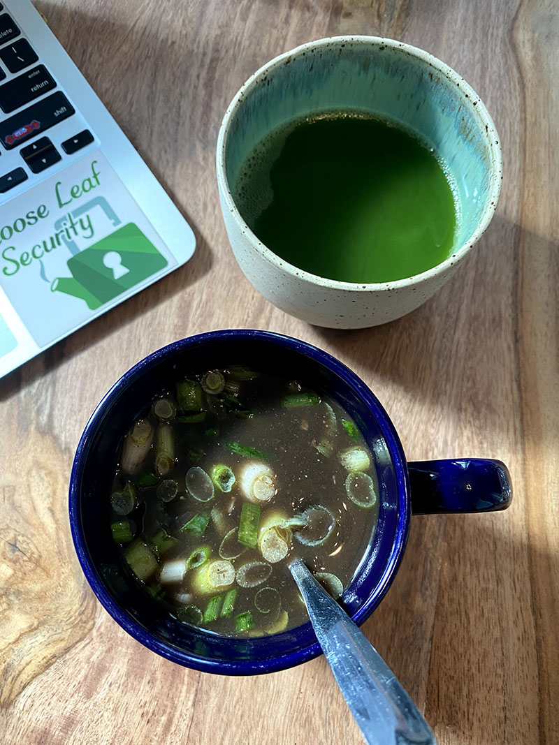 Photo of a handled mug of black bean broth miso soup with chopped scallions and a small ceramic cup without a handle with matcha