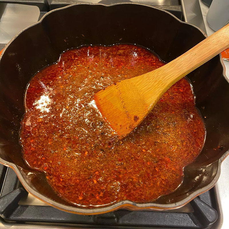 Photo of mapo tofu in progress: mushroom broth has just been added to the paste. It's bright red.