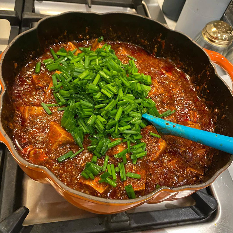Photo of mapo tofu in progress: chives are piled on top of the tofu with reduced and thickened sauce.