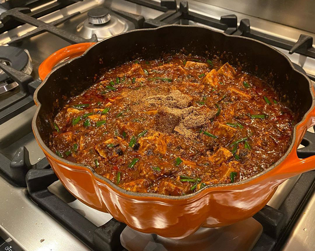 Photo of finished mapo tofu in a pumpkin-shaped Dutch oven, ground toasted Sichuan pepper on top but not yet mixed in.