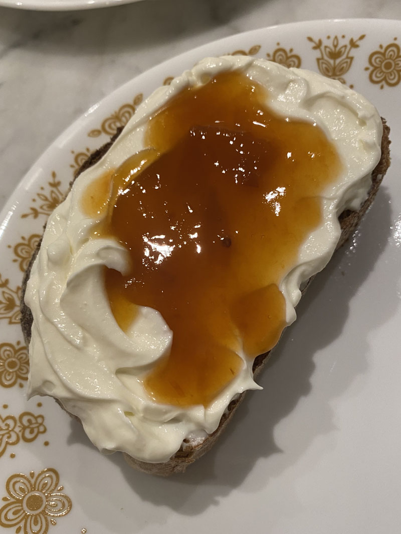 Photo of a piece of toast topped with whipped ricotta and a muted orange greengage plum jam on a plate