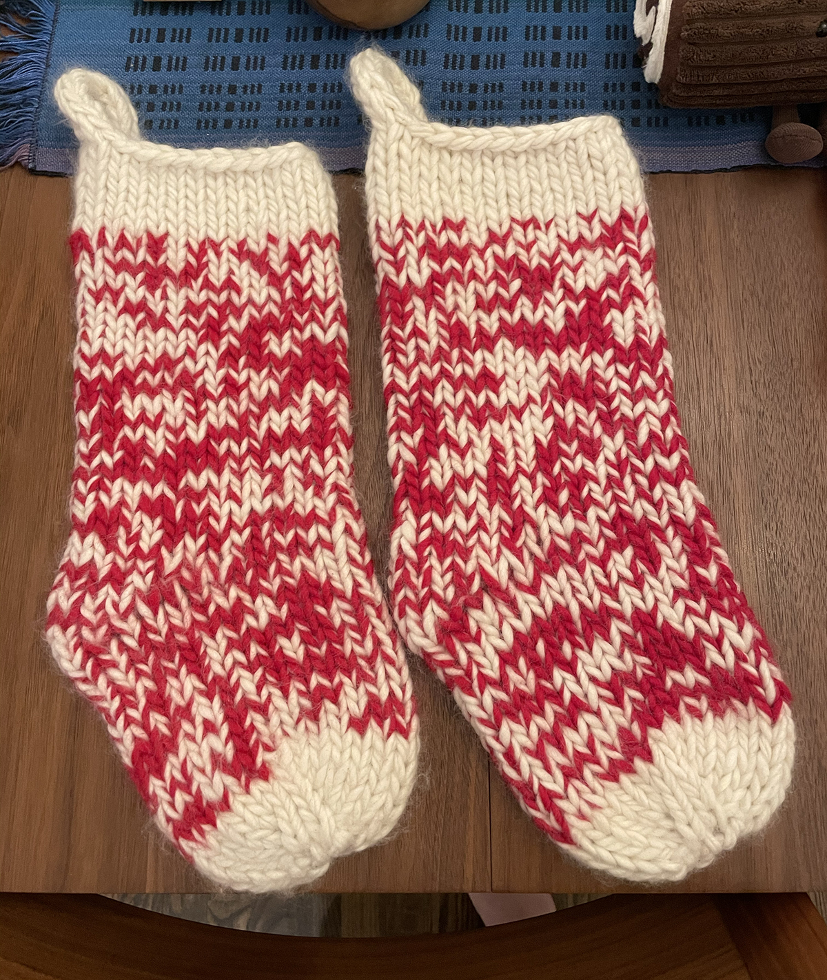 Two completed Snow Day Stockings: The toes and tops are a creamy white, and the main section of the body is a marled bright red and creamy white. The stitches are very defined due to the large needle size and single-ply nature of the yarn. They have an i-cord loop incorporated in the bind-off for hanging.