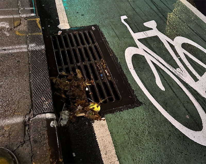 This catch basin grate occupies part of the bike lane path and has raised sections parallel to the direction a bike travels in the lane. Bike tires and wheels of a similar width can get stuck when riding on these grates.